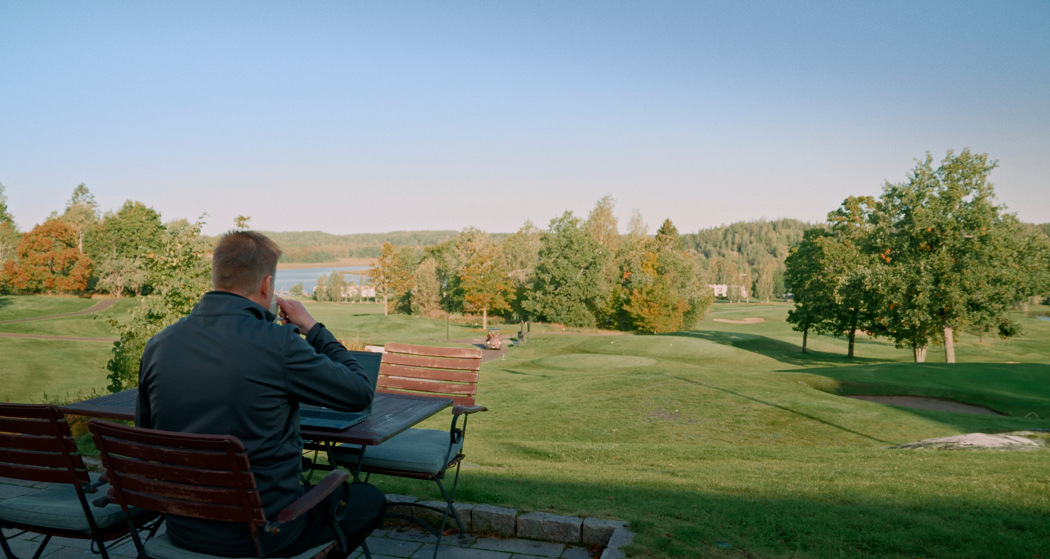 Mies tekee töitä läppärillä ja nauttii golfkentän merellisistä maisemista.